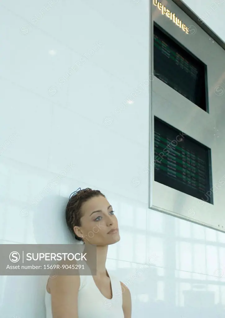 Woman leaning against wall below arrival and departure boards
