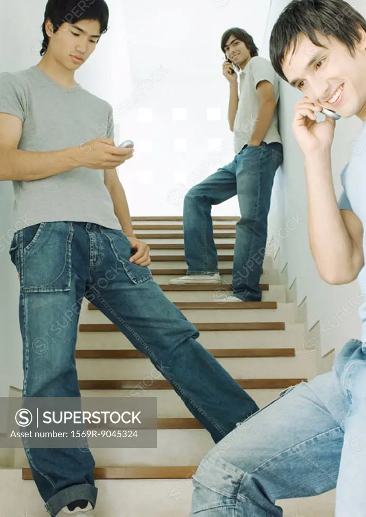 Three young men using cell phones in stairway