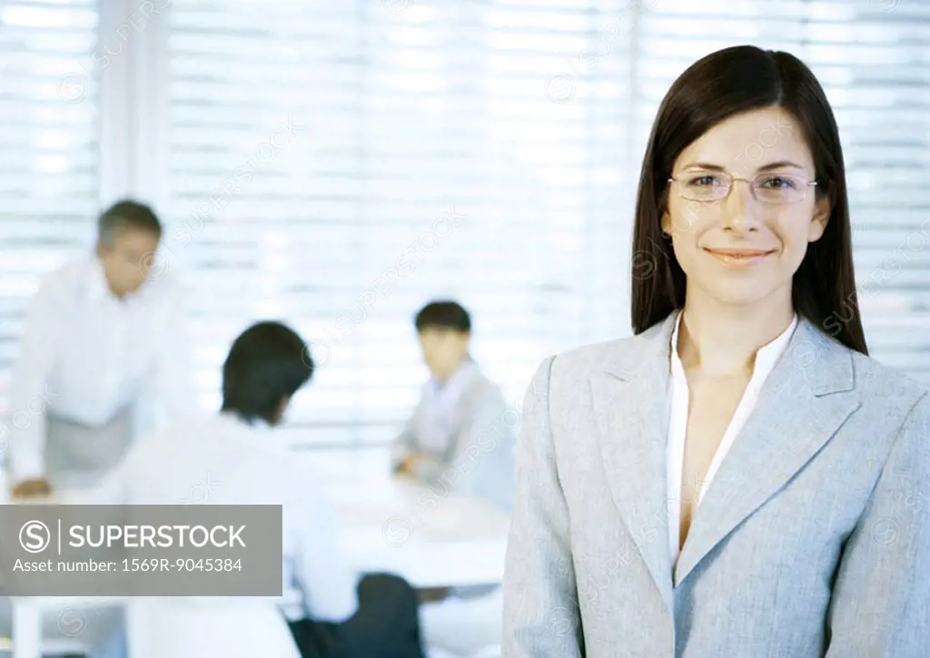 Businesswoman smiling at camera, people working in office in background