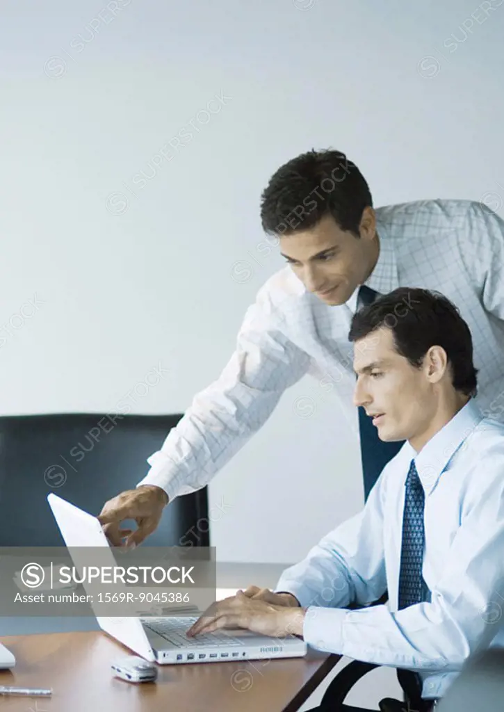 Businessman leaning over colleague´s shoulder pointing at laptop screen