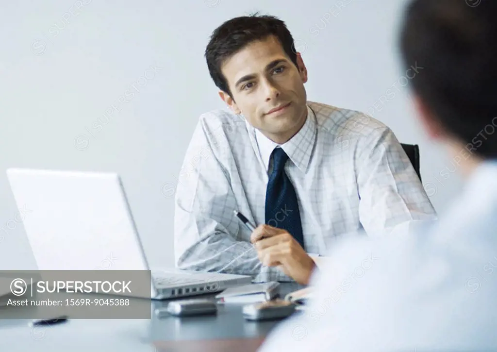 Businessman sitting at desk looking at second man