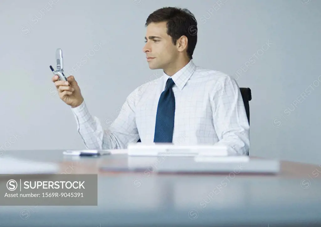 Businessman sitting at desk looking at cell phone