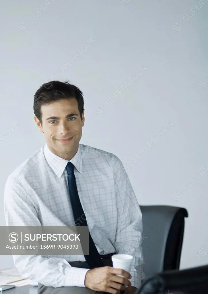 Businessman in office, holding cup and smiling at camera