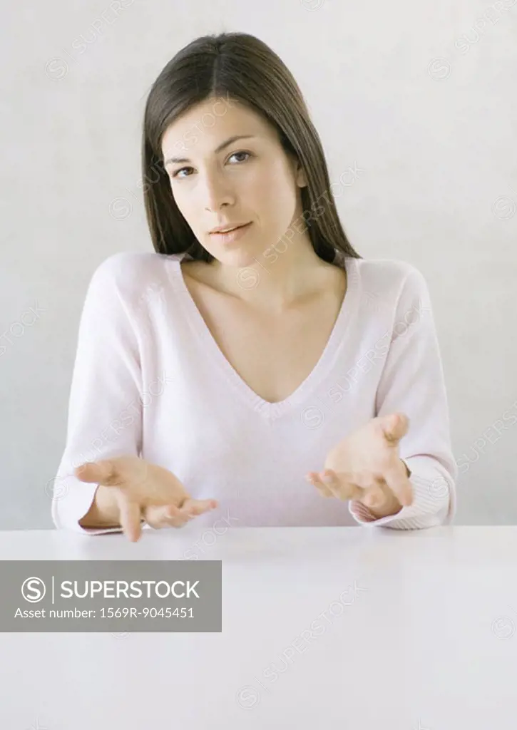 Woman sitting at table gesturing, looking at camera