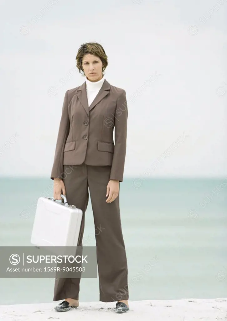 Businesswoman standing on beach holding briefcase