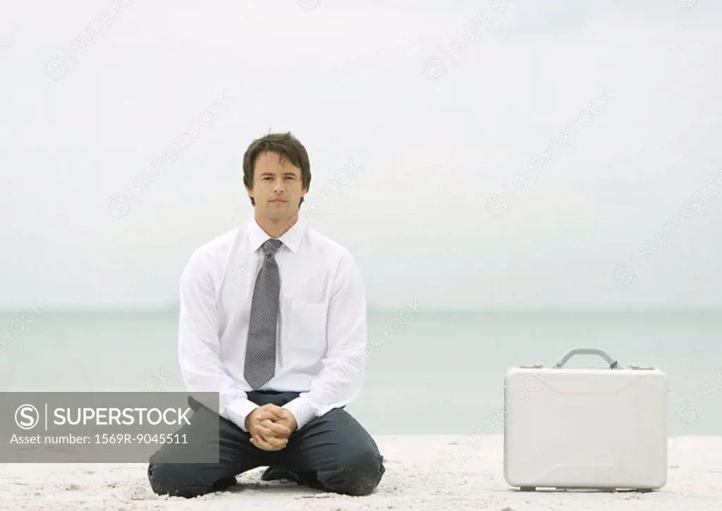 Businessman kneeling on beach next to briefcase