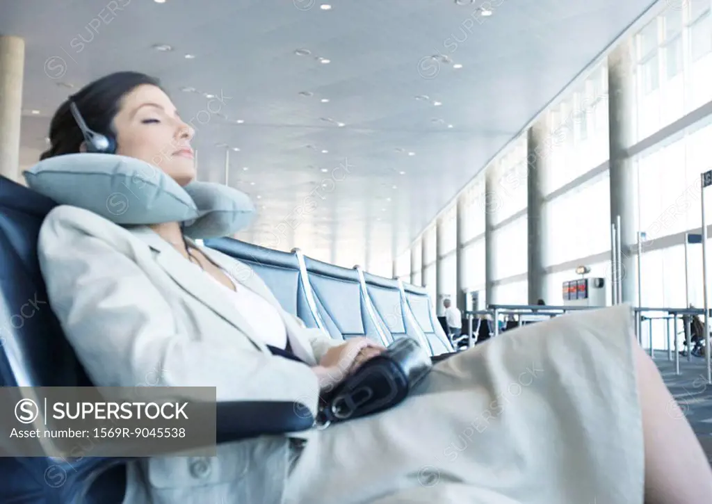 Business traveler sitting in airport lounge, napping with neck pillow