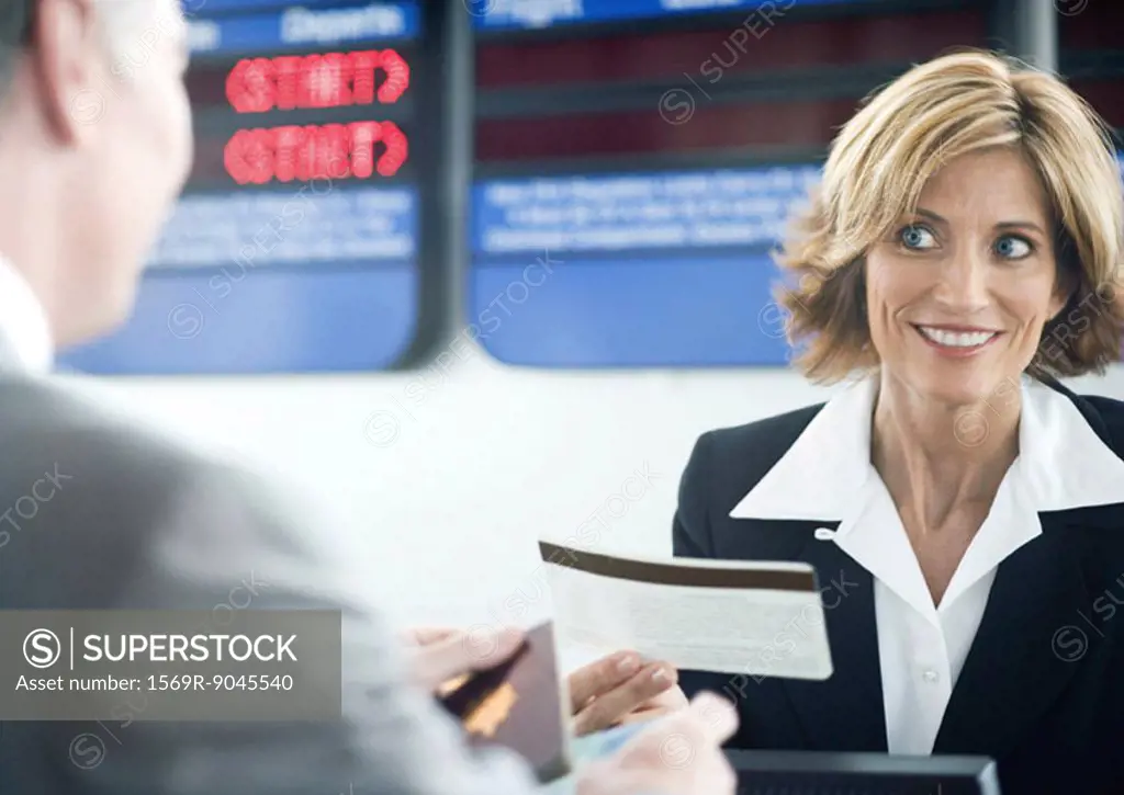 Airline attendant handing passenger ticket at check-in counter
