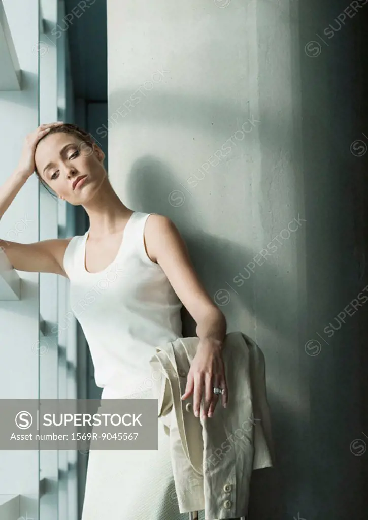 Woman standing near window, holding head