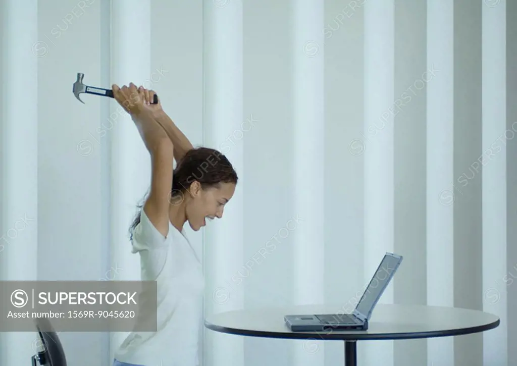 Woman shouting and swinging hammer at laptop