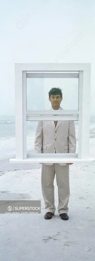 Businessman standing behind window frame on beach