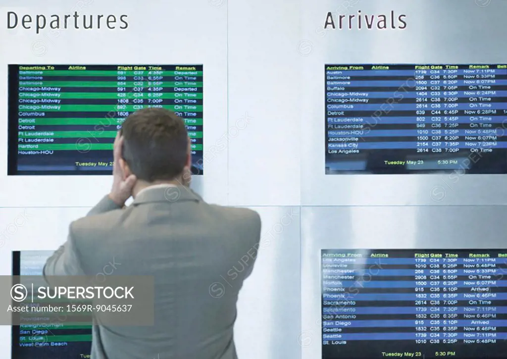 Businessman looking at departure board, holding head, rear view