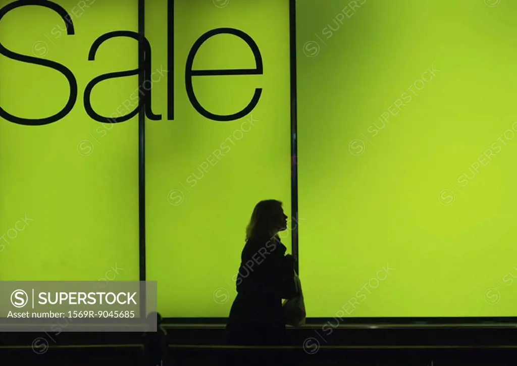 Sale sign in shop window and silhouette of passer-by