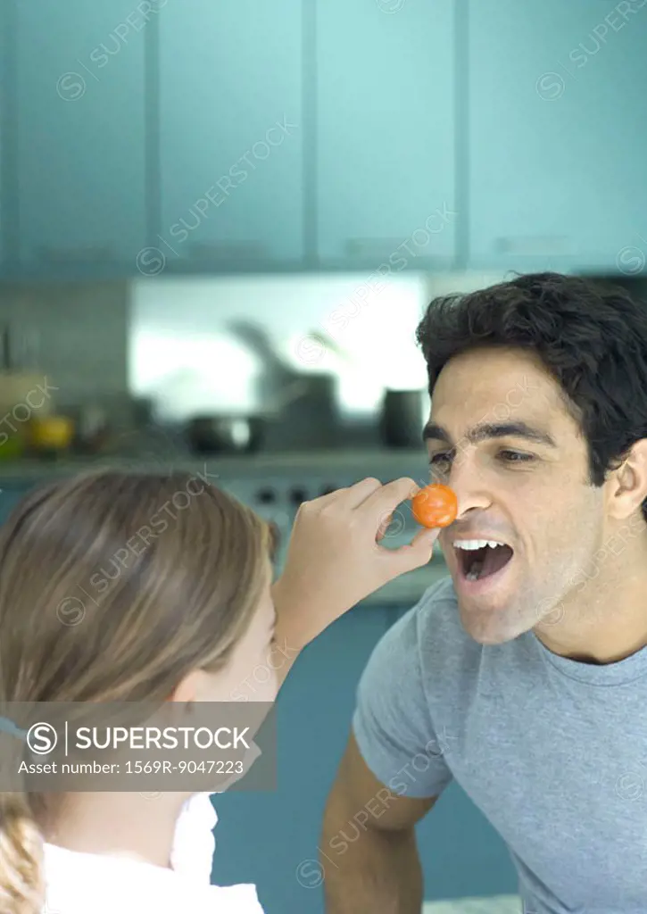 Girl holding up cherry tomato to man´s nose