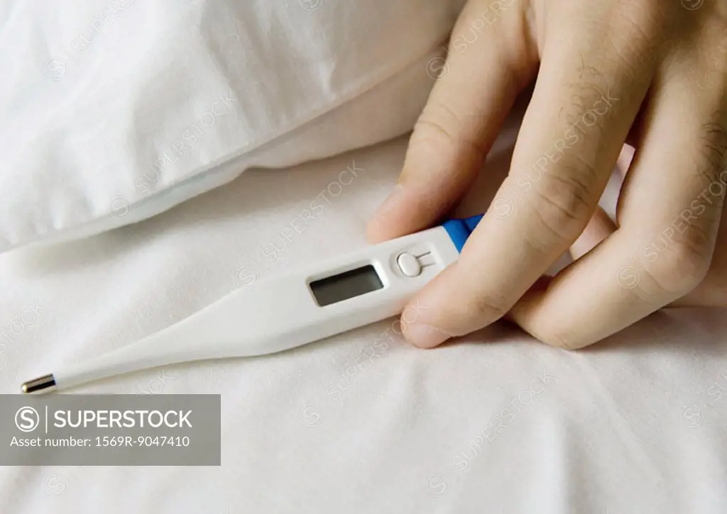 Man´s hand holding thermometer on bed