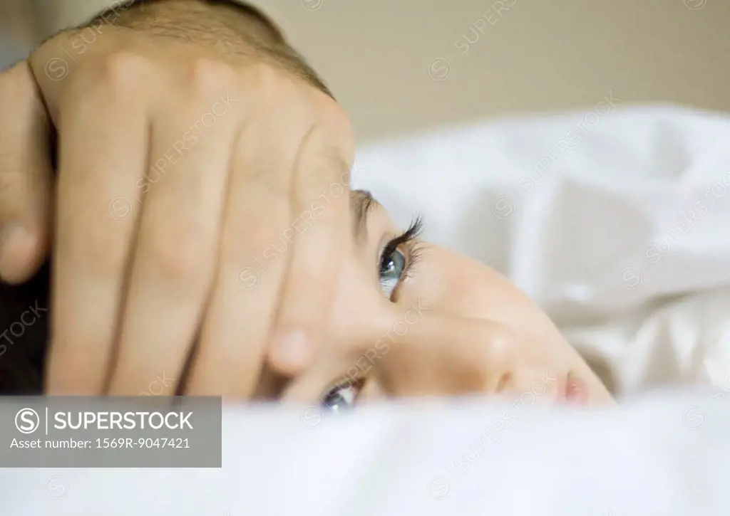Child lying in bed with father´s hand on forehead