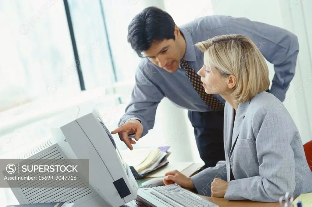 Businessman leaning over female colleague´s shoulder pointing at monitor