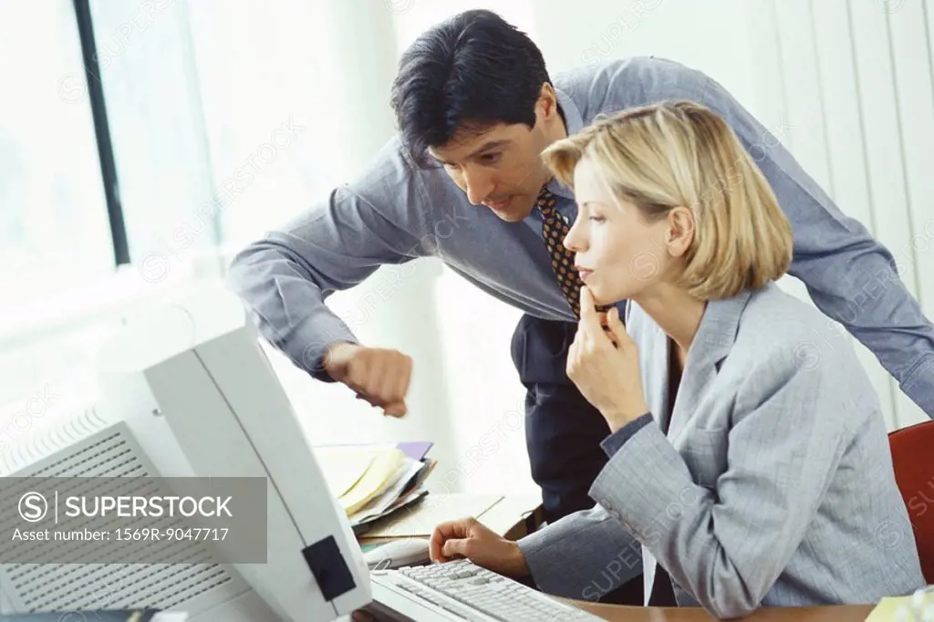 Businessman leaning over female colleague´s shoulder looking at monitor