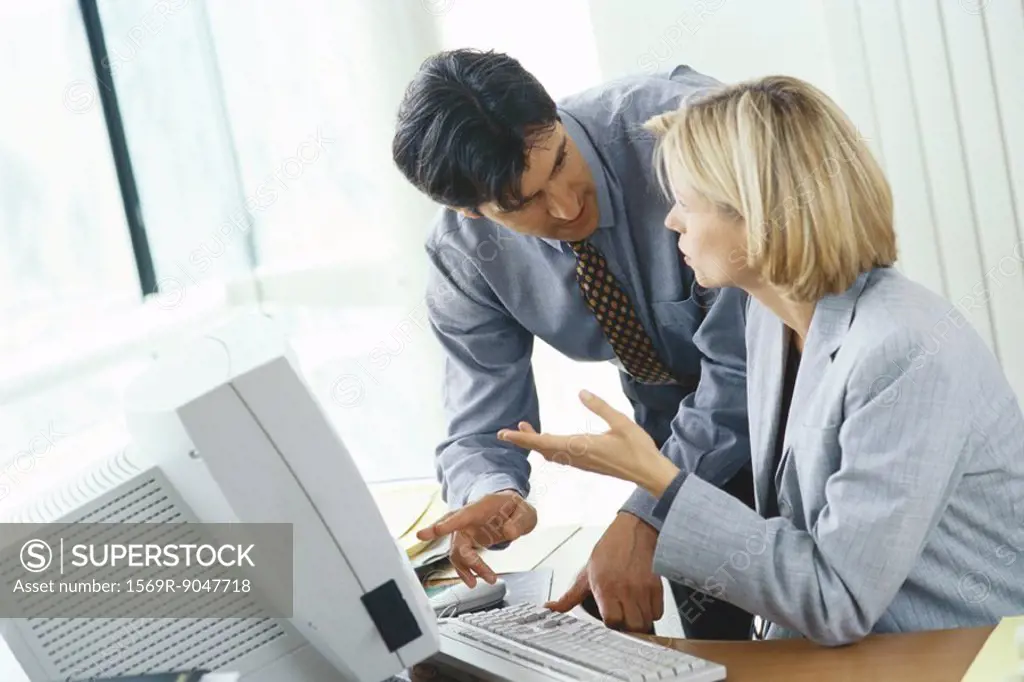 Businessman leaning over female colleague´s shoulder pointing at monitor