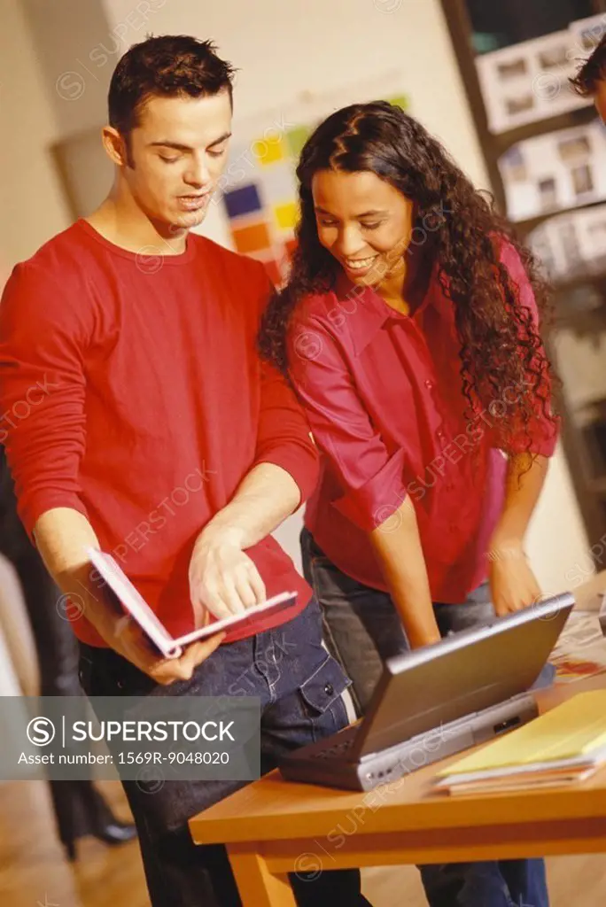 Young man and woman standing next to laptop, man pointing to user´s manual