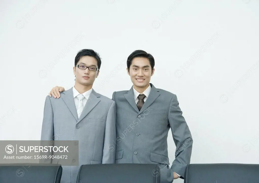 Two businessmen, one standing with arm around the other´s shoulders, smiling at camera