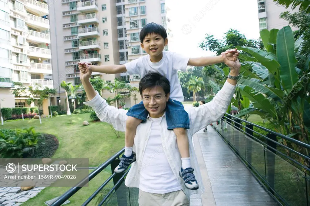 Boy riding on father´s shoulders, front view, smiling at camera