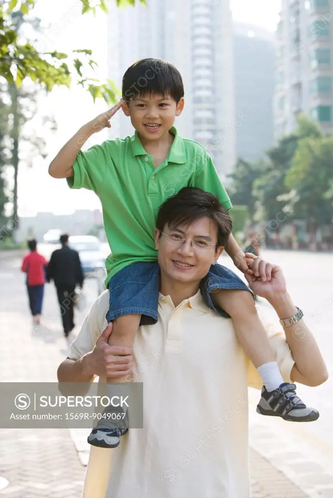 Boy riding on father´s shoulders, saluting camera