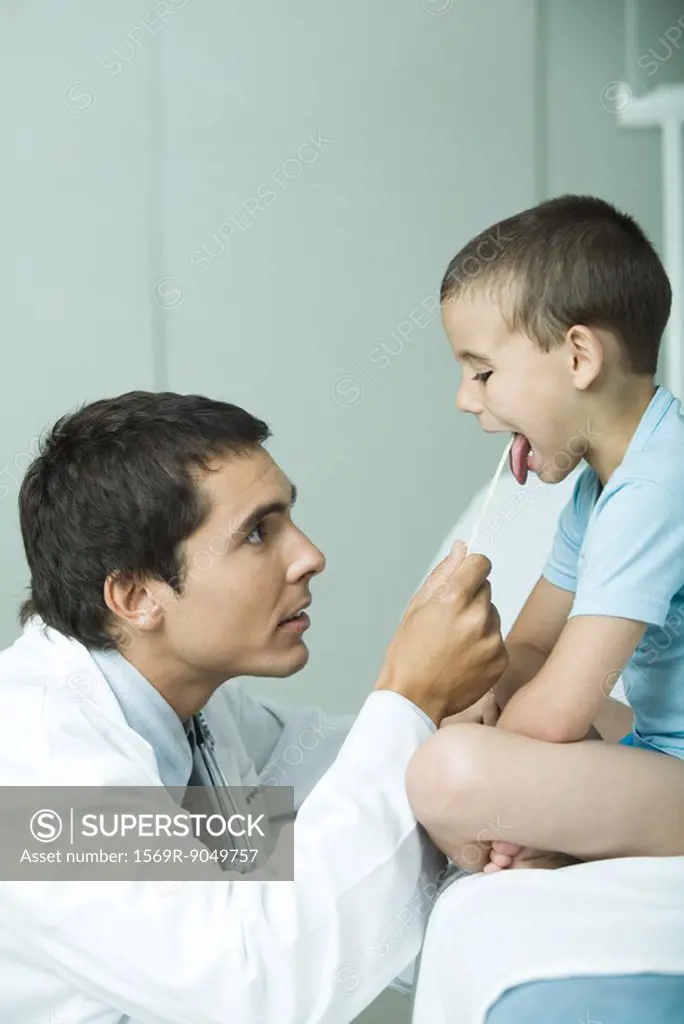Doctor holding down boy´s tongue with tongue depressor