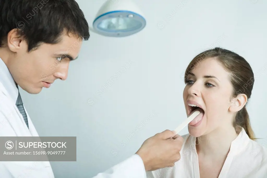 Doctor holding down woman´s tongue with tongue depressor