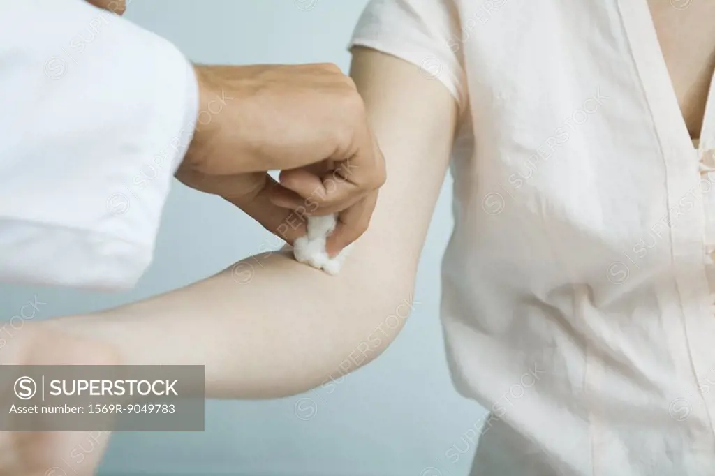 Doctor cleaning woman´s arm with cotton ball