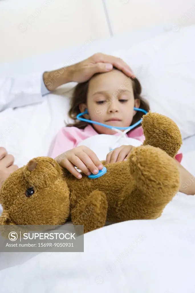 Child holding toy stethoscope to teddy bear, doctor feeling child´s forehead