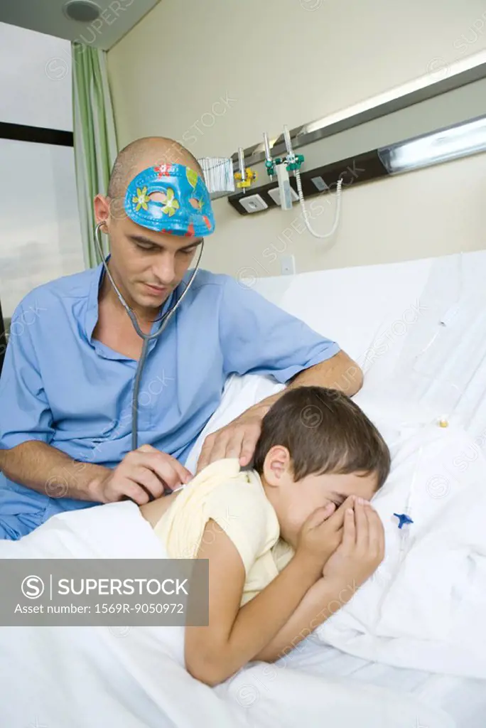 Boy lying in hospital bed, doctor listening to boy´s back with stethoscope