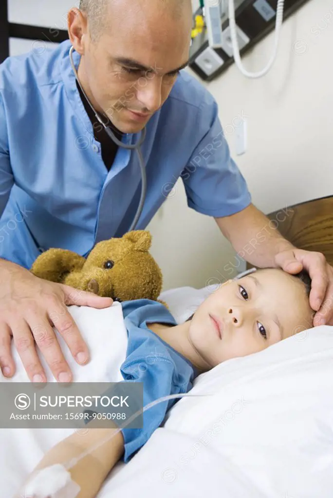 Girl lying in hospital bed, male nurse´s hand on girl´s forehead