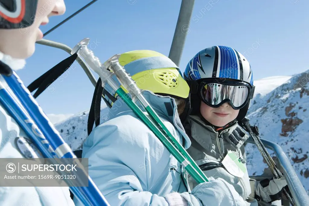 Young skiers on chair lift, one whispering in the other´s ear