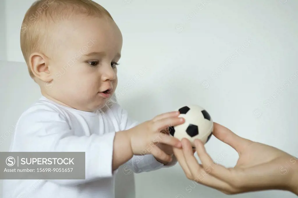 Baby taking ball from mother´s hand, close-up