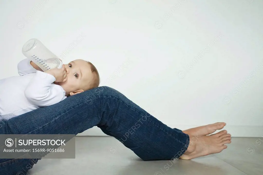 Baby lying on mother´s legs, drinking from bottle, side view