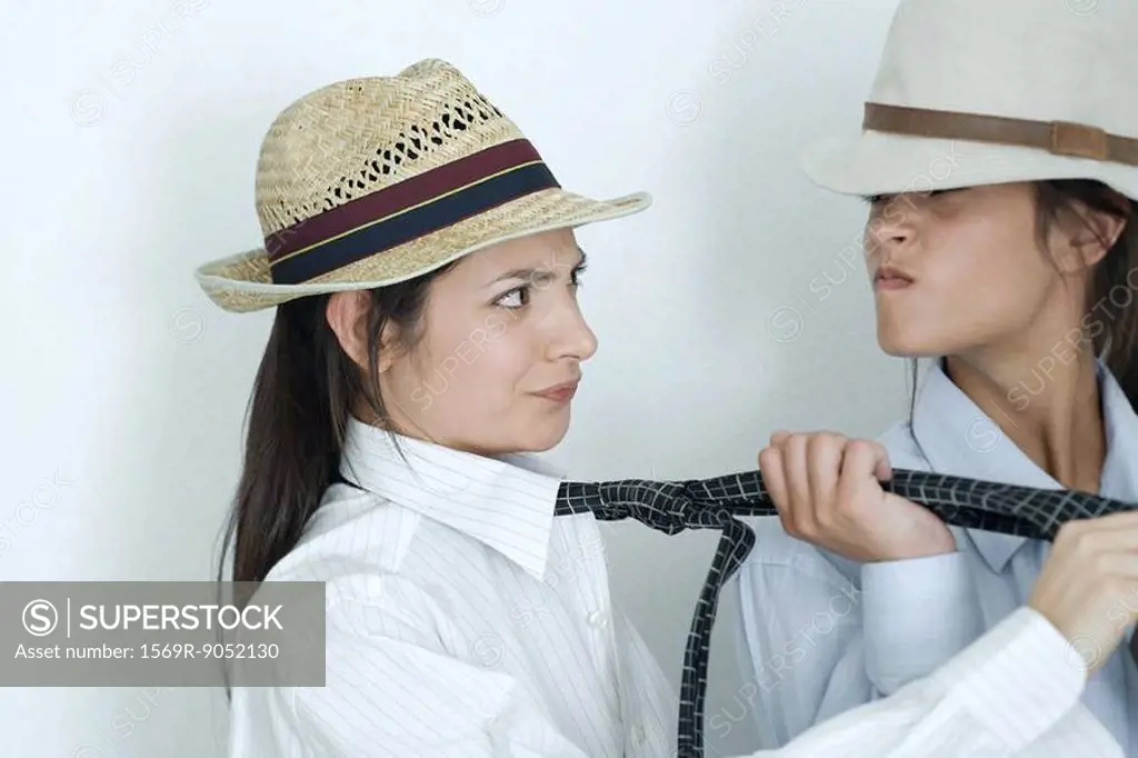 Two young female friends dressed in button down shirts, ties and hats, one pulling on the other´s tie