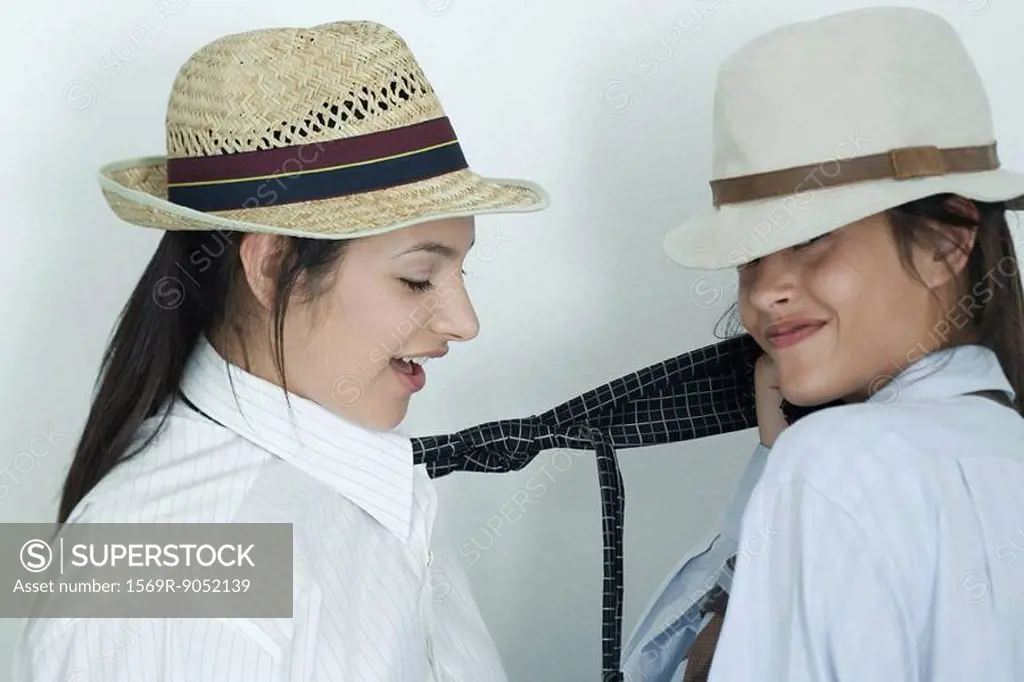 Two young female friends dressed in button down shirts, ties and hats, one pulling on the other´s tie, portrait