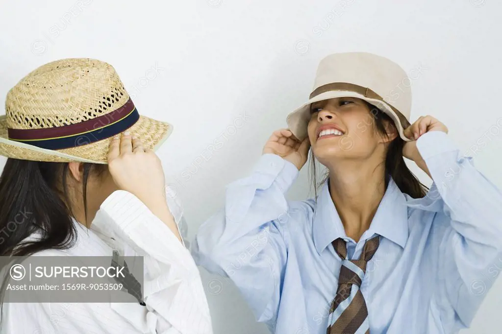 Two young female friends wearing men´s clothing and putting on hats