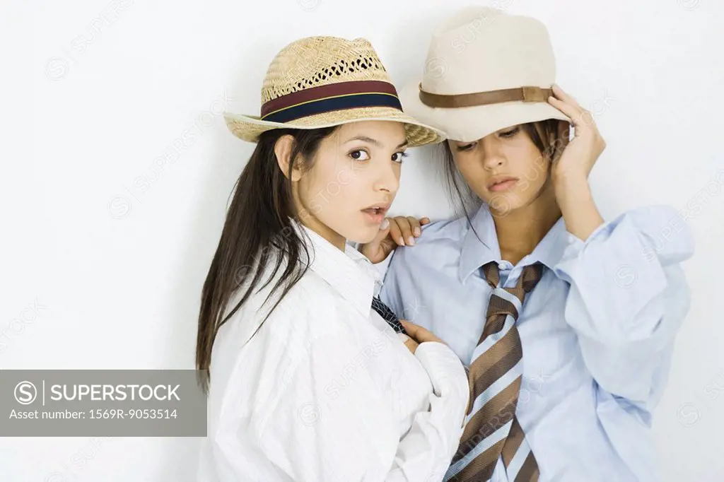 Two young females dressed in men´s clothing and hats, one looking at camera