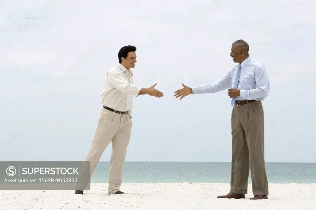 Two businessmen standing on the beach, reaching out to shake each other´s hands