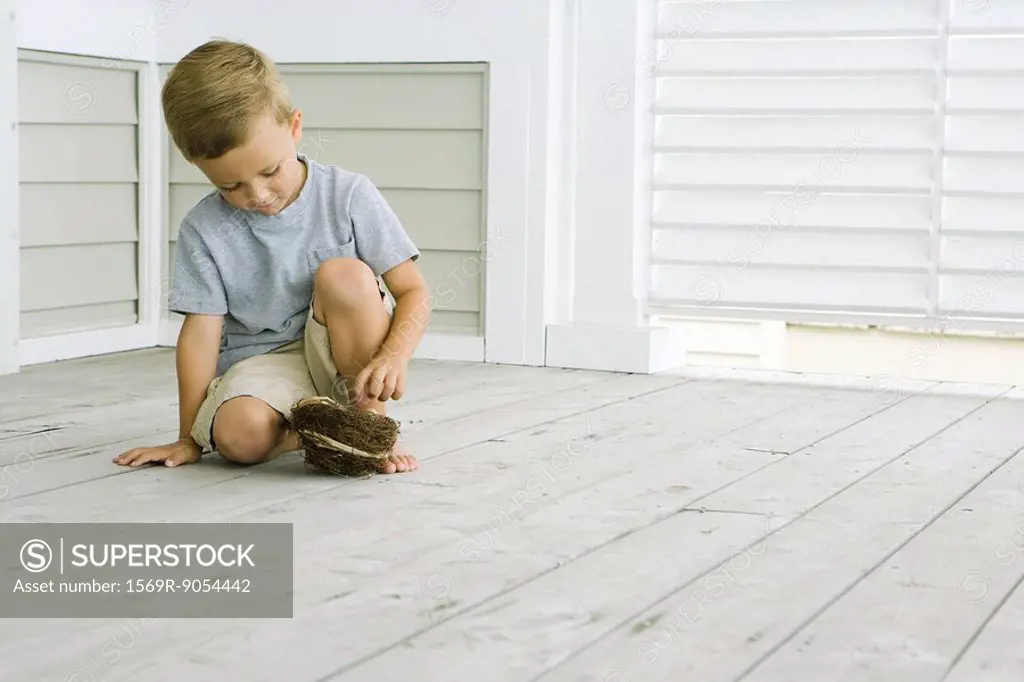 Boy crouching on the ground, touching bird´s nest, looking down