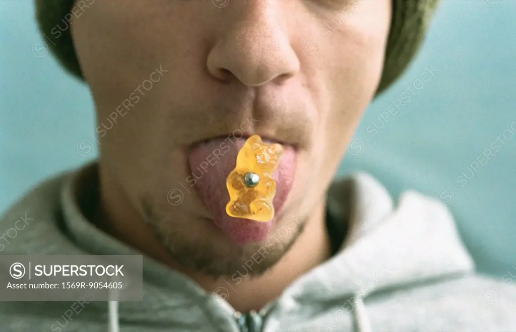 Man sticking out pierced tongue, piercing holding candy bear