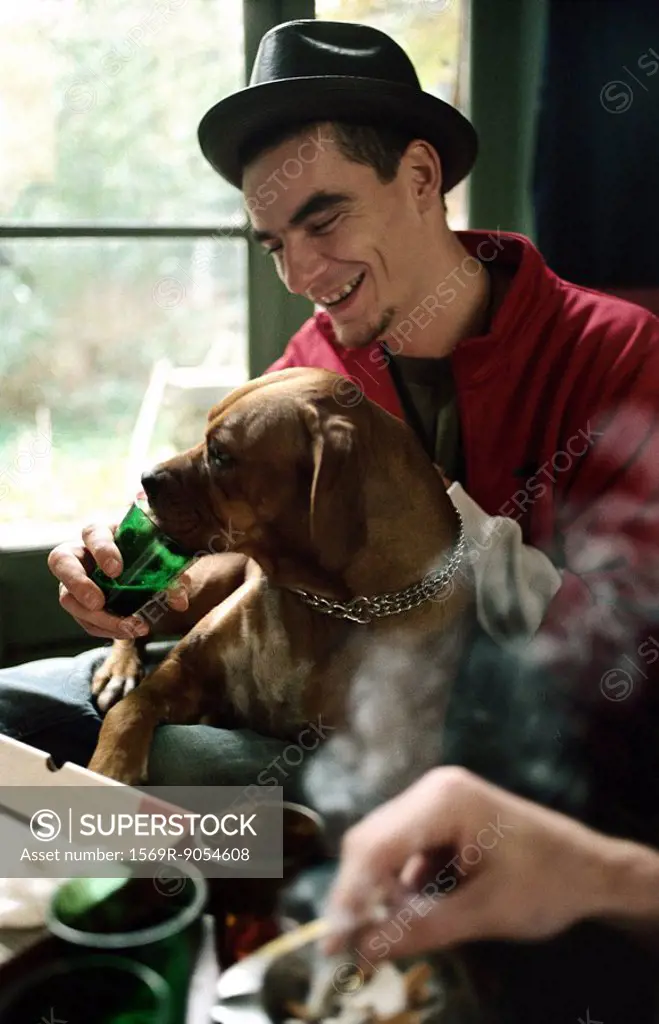 Young man letting pet dog drink from glass