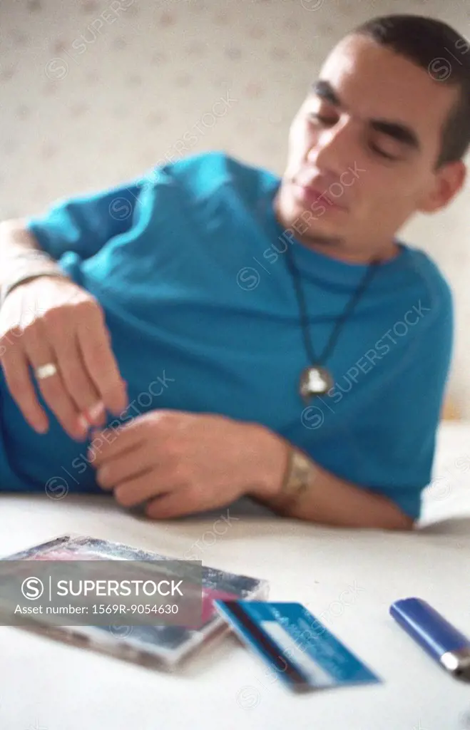 Young man reclining on bed smoking, line of cocaine on cd case in foreground