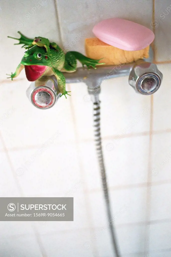 Plastic toy frog, sponge, pink bar of soap set on shower faucet