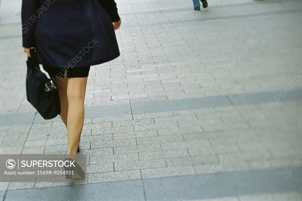 Businesswoman walking on sidewalk, rear view, cropped