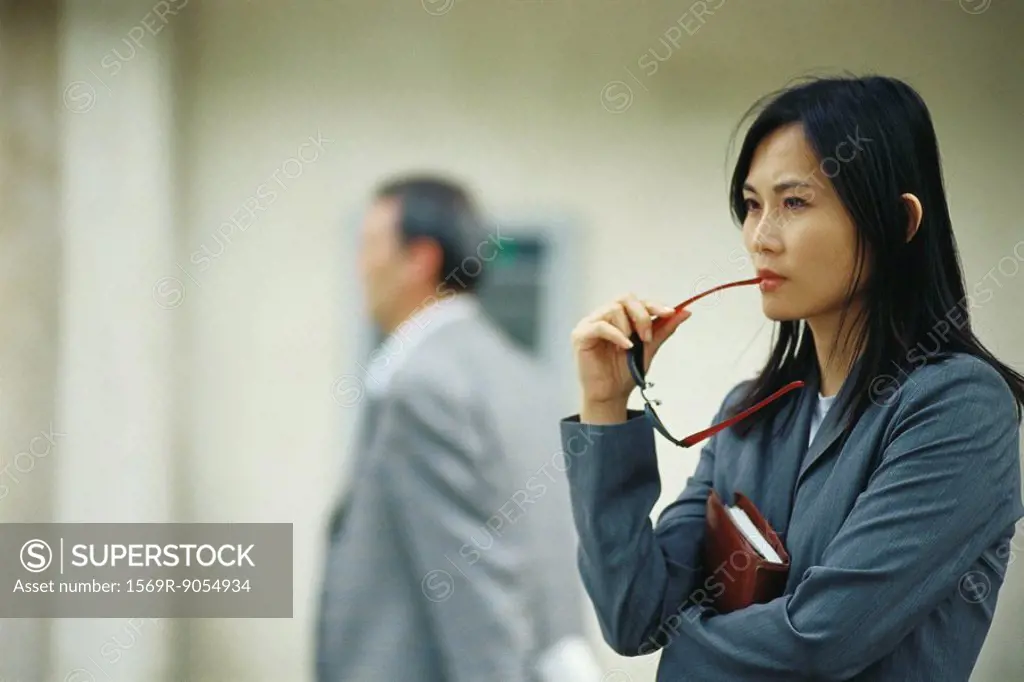 Businesswoman waiting in lobby, holding sunglasses against mouth