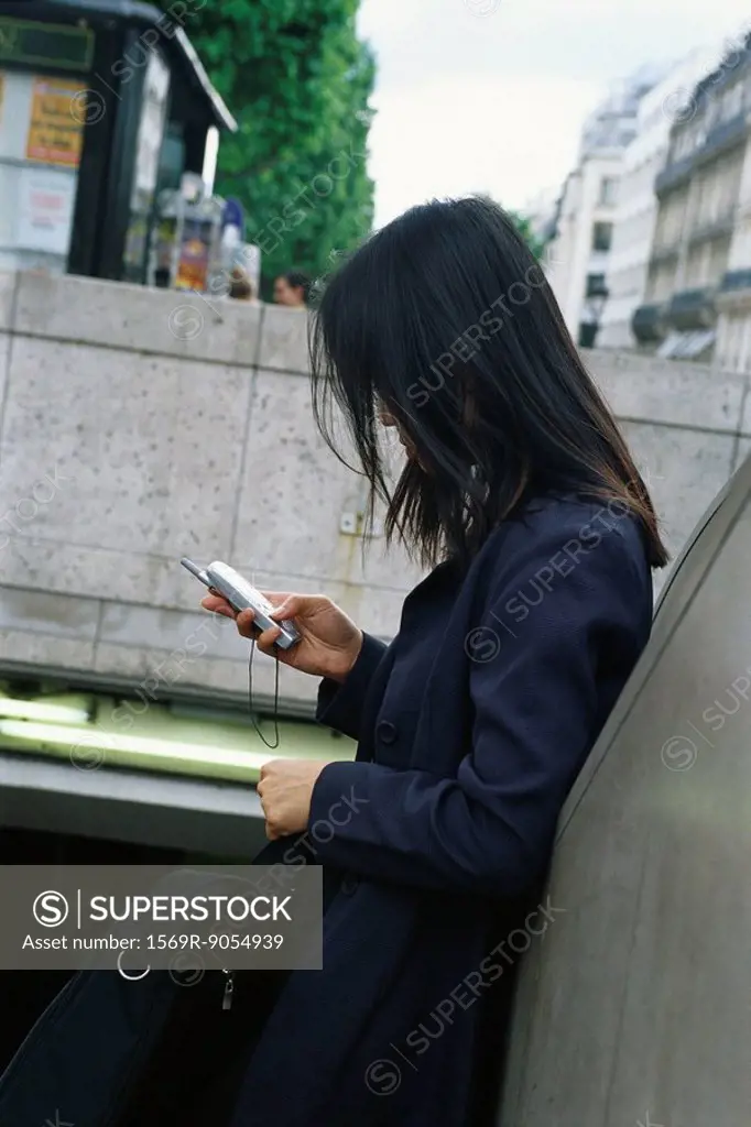 Businesswoman leaning against wall, looking at cell phone