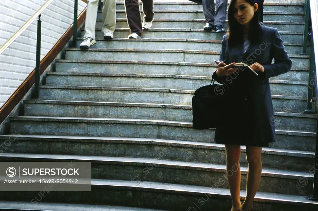 Businesswoman standing at bottom of steps, holding open agenda